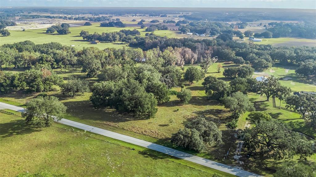 An aerial view shows a paved road cutting through a large, grassy, tree-filled rural landscape — TRACT 3 - CR 221, WILDWOOD, FL