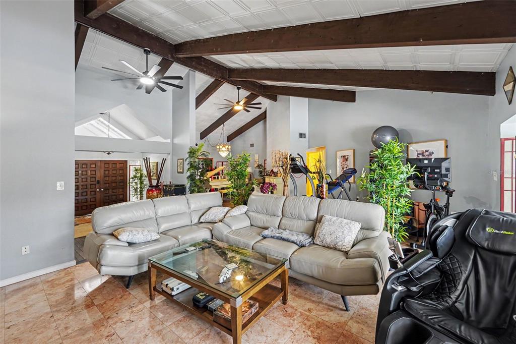 A spacious living room features vaulted ceilings with exposed beams, tile flooring, and a sectional sofa — 1615 SAINT PAULS DRIVE, CLEARWATER, FL