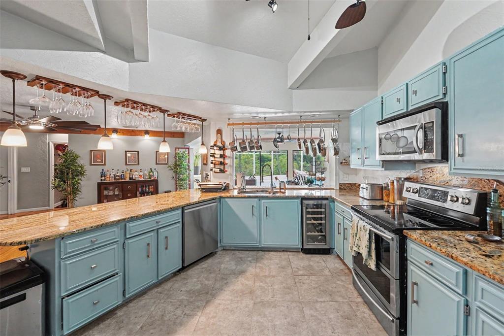 A kitchen features light blue cabinets, granite countertops, a hanging pot rack, and tile flooring — 1615 SAINT PAULS DRIVE, CLEARWATER, FL