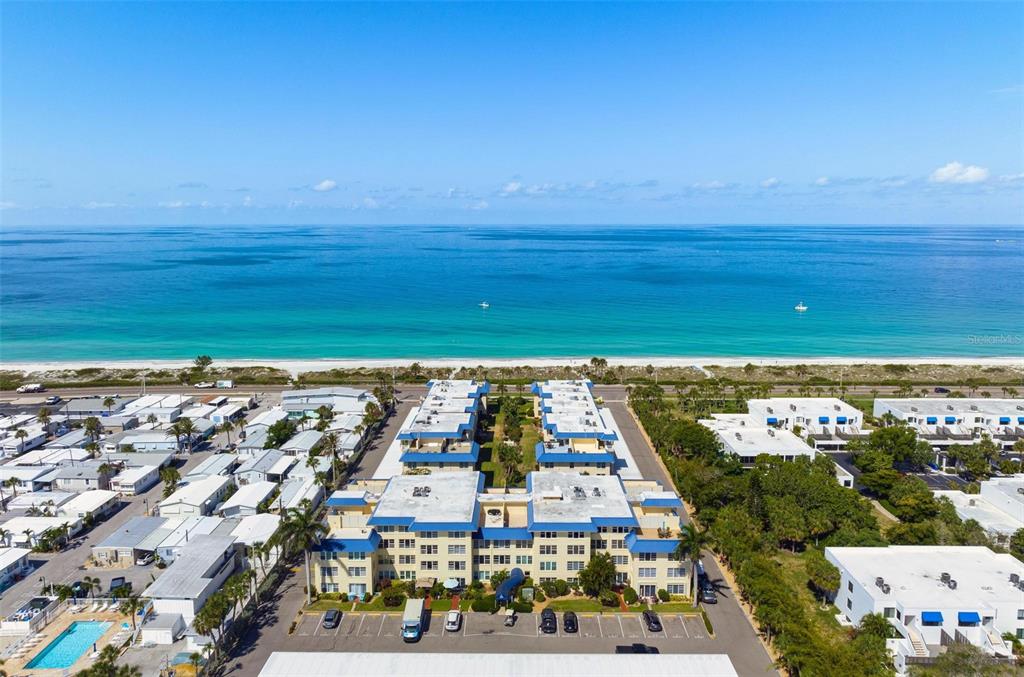 An aerial view shows a multi-story apartment complex situated directly across from a sandy beach — 3806 GULF OF MEXICO DRIVE UNIT C211, LONGBOAT KEY, FL