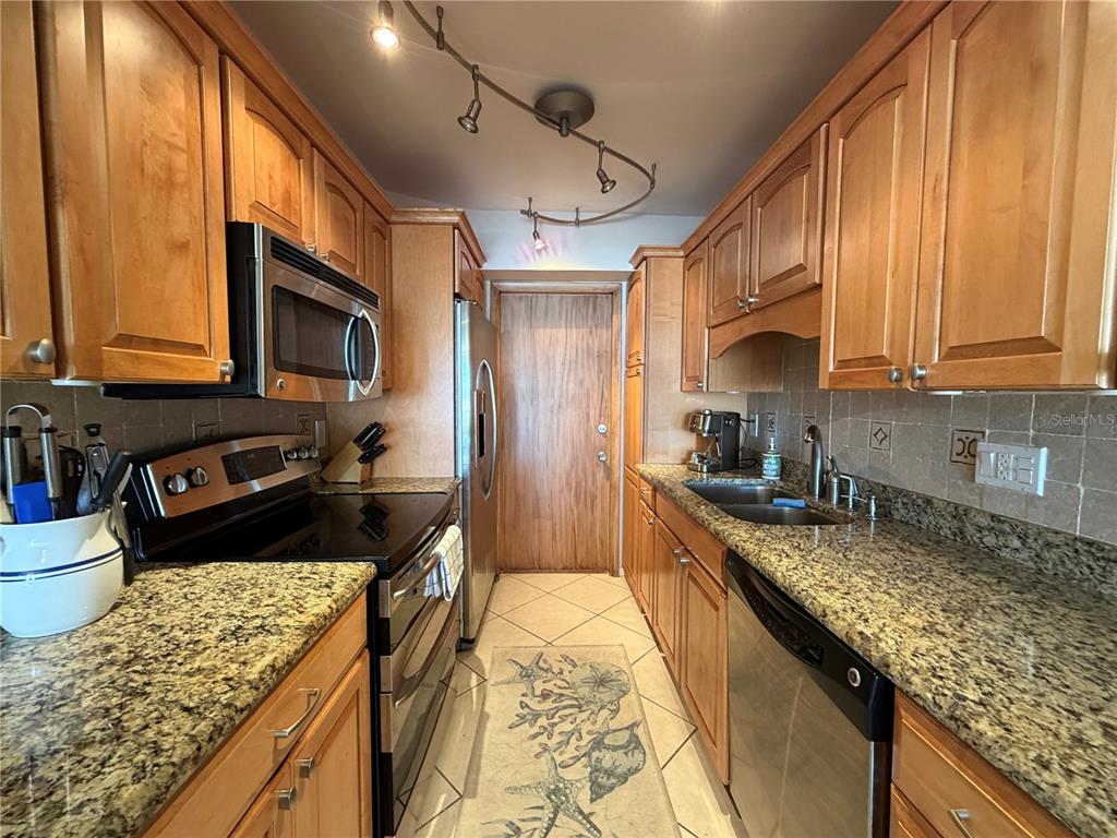 A galley kitchen features wood cabinets, granite countertops, stainless steel appliances, and tile flooring — 3806 GULF OF MEXICO DRIVE UNIT C211, LONGBOAT KEY, FL