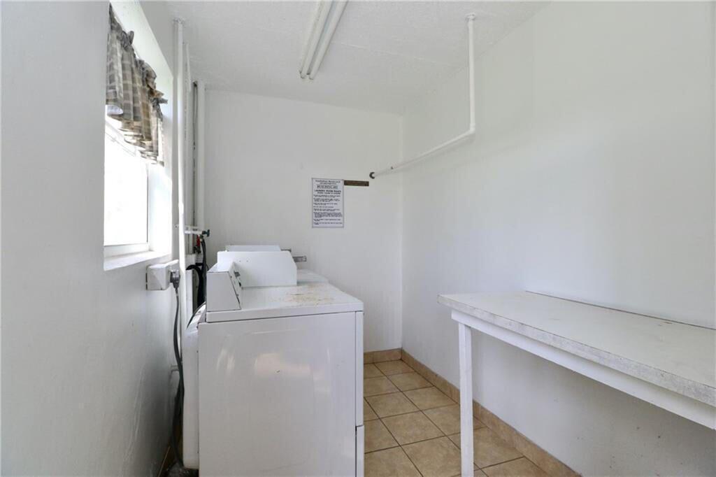 A laundry room features a white washing machine, a folding table, and tiled flooring — 9915 Sandalfoot Boulevard # 408, Boca Raton FL 33428, BOCA RATON, FL