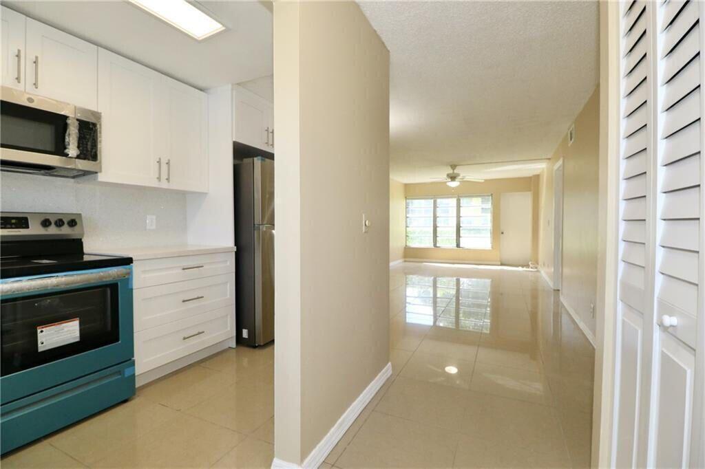 A kitchen with white cabinets and stainless steel appliances opens into a bright living area — 9915 Sandalfoot Boulevard # 408, Boca Raton FL 33428, BOCA RATON, FL