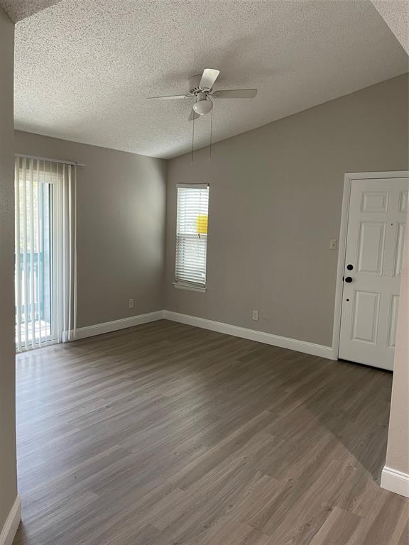 An empty living room features light gray walls, wood-look flooring, a ceiling fan, and blinds — 3764 IDLEBROOK CIRCLE UNIT 204, CASSELBERRY, FL