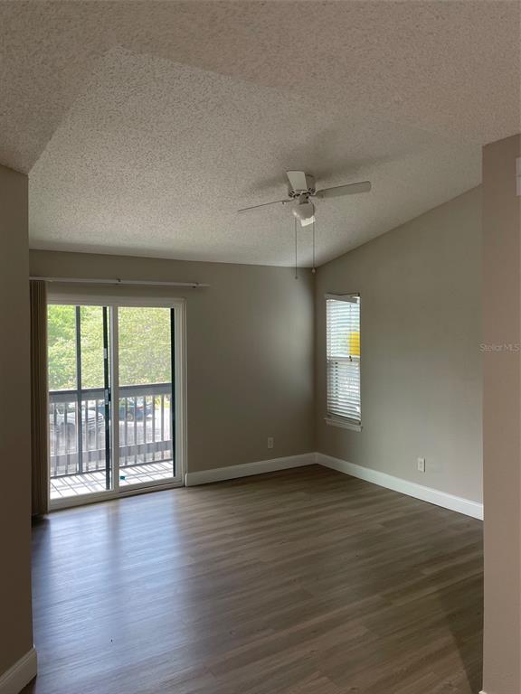 An empty living room features light wood-look flooring, a ceiling fan, and a sliding glass door — 3764 IDLEBROOK CIRCLE UNIT 204, CASSELBERRY, FL