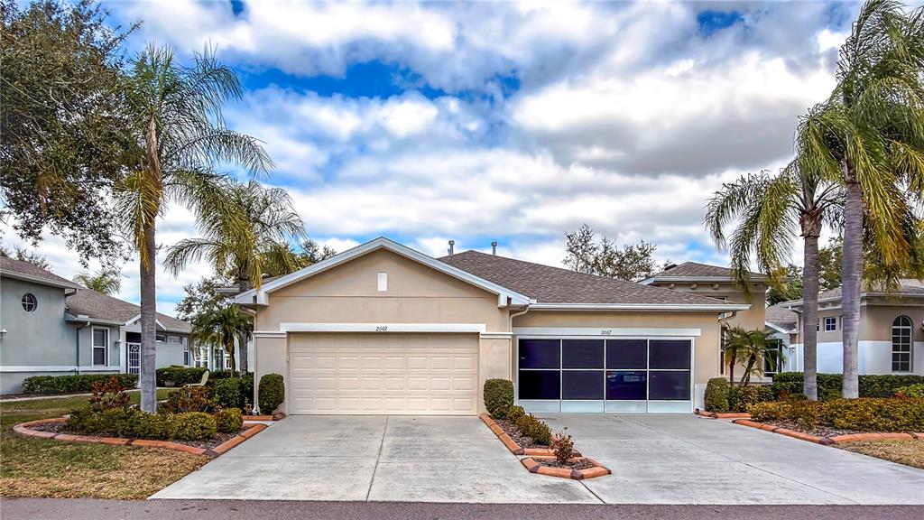A beige single-story house features a two-car garage, a screened-in area, and palm trees — 2069 SIFIELD GREENS WAY UNIT 102, SUN CITY CENTER, FL
