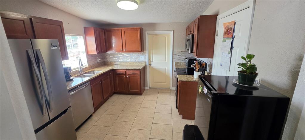 A kitchen features wood cabinets, granite countertops, stainless steel appliances, and light-colored tile flooring — 3609 SCHWALBE DRIVE, SARASOTA, FL