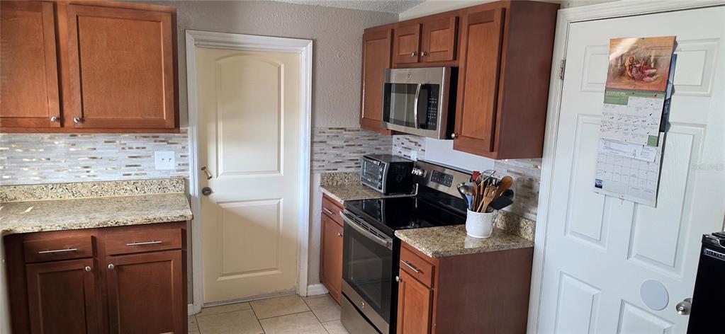 A kitchen features wood cabinets, granite countertops, a tiled backsplash, and stainless steel appliances — 3609 SCHWALBE DRIVE, SARASOTA, FL