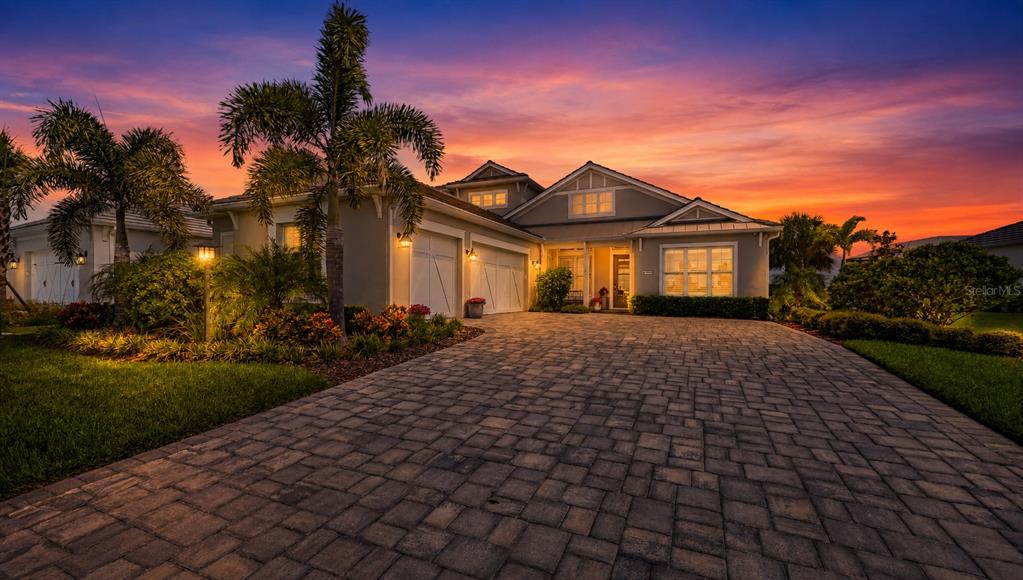 A paved driveway leads to a suburban house exterior at sunset with palm trees — 7919 WATERBEND TRAIL, SARASOTA, FL