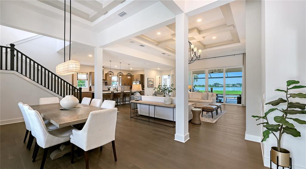 An open-concept living and dining area features coffered ceilings, hardwood floors, and a waterfront view — 7919 WATERBEND TRAIL, SARASOTA, FL