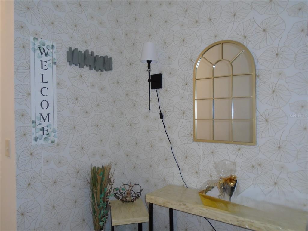 A small entryway features patterned wallpaper, a wall-mounted lamp, a mirror, and two console tables — 1991 HEMINGWAY CIRCLE, GROVELAND, FL