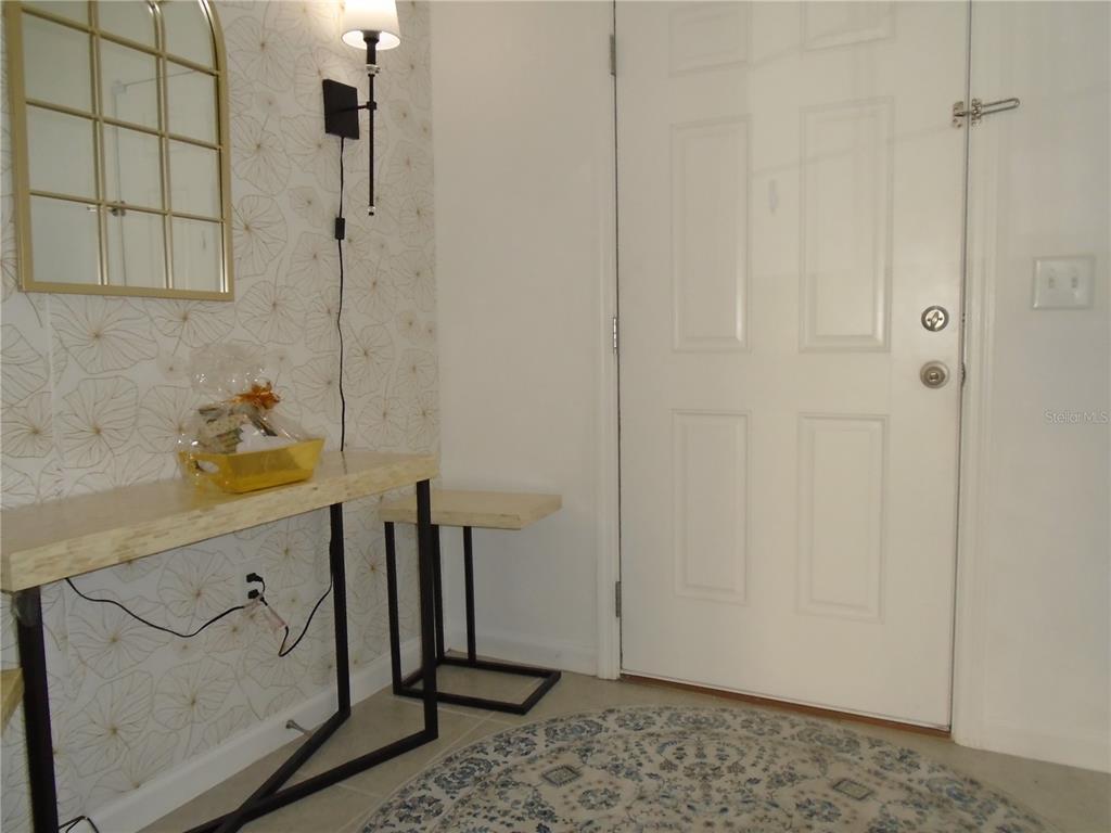 An entryway features a console table, patterned wallpaper, a wall sconce, and a front door — 1991 HEMINGWAY CIRCLE, GROVELAND, FL