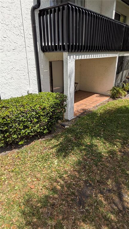 A ground-level patio sits beneath a second-story balcony next to a manicured hedge — 4401 S SEMORAN BOULEVARD UNIT 9, ORLANDO, FL