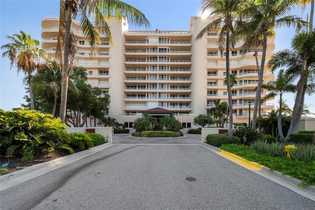 A multi-story beige residential building with balconies stands behind a paved driveway and palm trees — 3060 GRAND BAY BOULEVARD UNIT 133, LONGBOAT KEY, FL