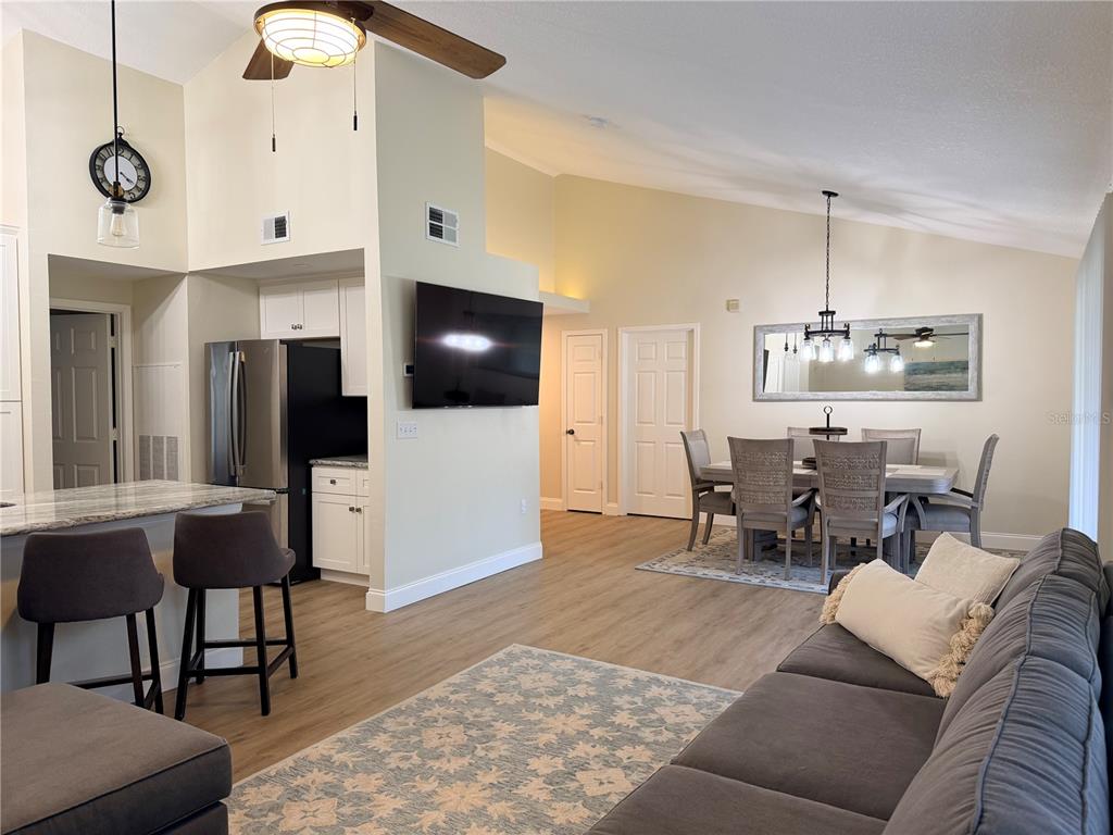 An open-concept living and dining area features light wood flooring, a kitchen, and vaulted ceilings — 10000 SW 52ND AVENUE UNIT 60, GAINESVILLE, FL