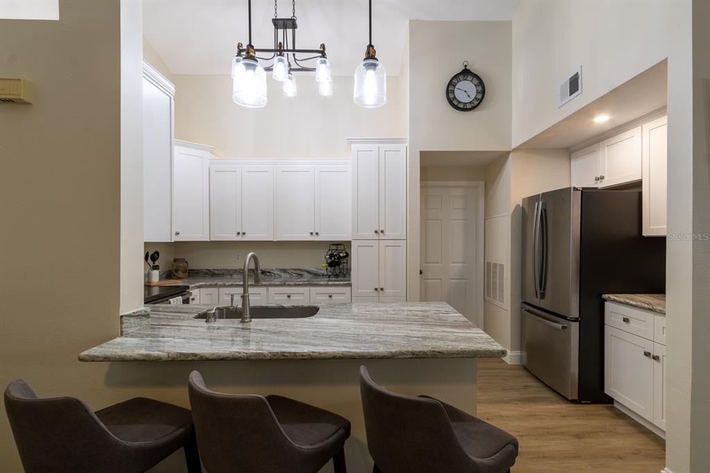 A kitchen features white cabinets, granite countertops, a breakfast bar with stools, and stainless appliances — 10000 SW 52ND AVENUE UNIT 60, GAINESVILLE, FL