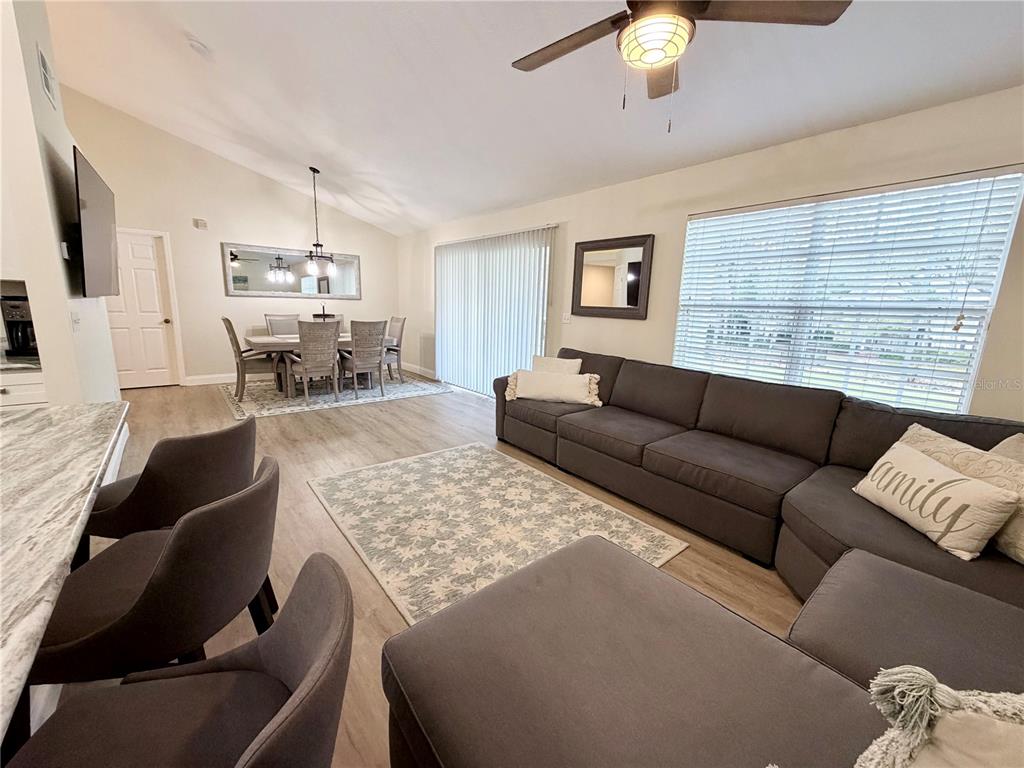 An open-concept living and dining area features light wood flooring, a gray sectional, and neutral walls — 10000 SW 52ND AVENUE UNIT 60, GAINESVILLE, FL