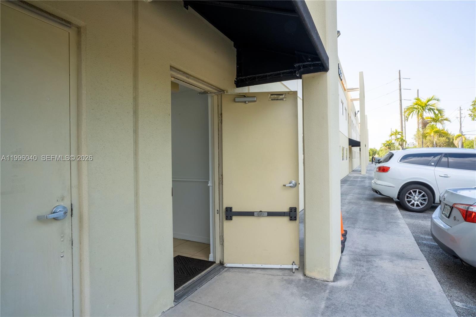 An open door leads into a commercial space with a concrete walkway and parked cars — 10800 NW 21St # 190, Doral FL 33172, DORAL, FL