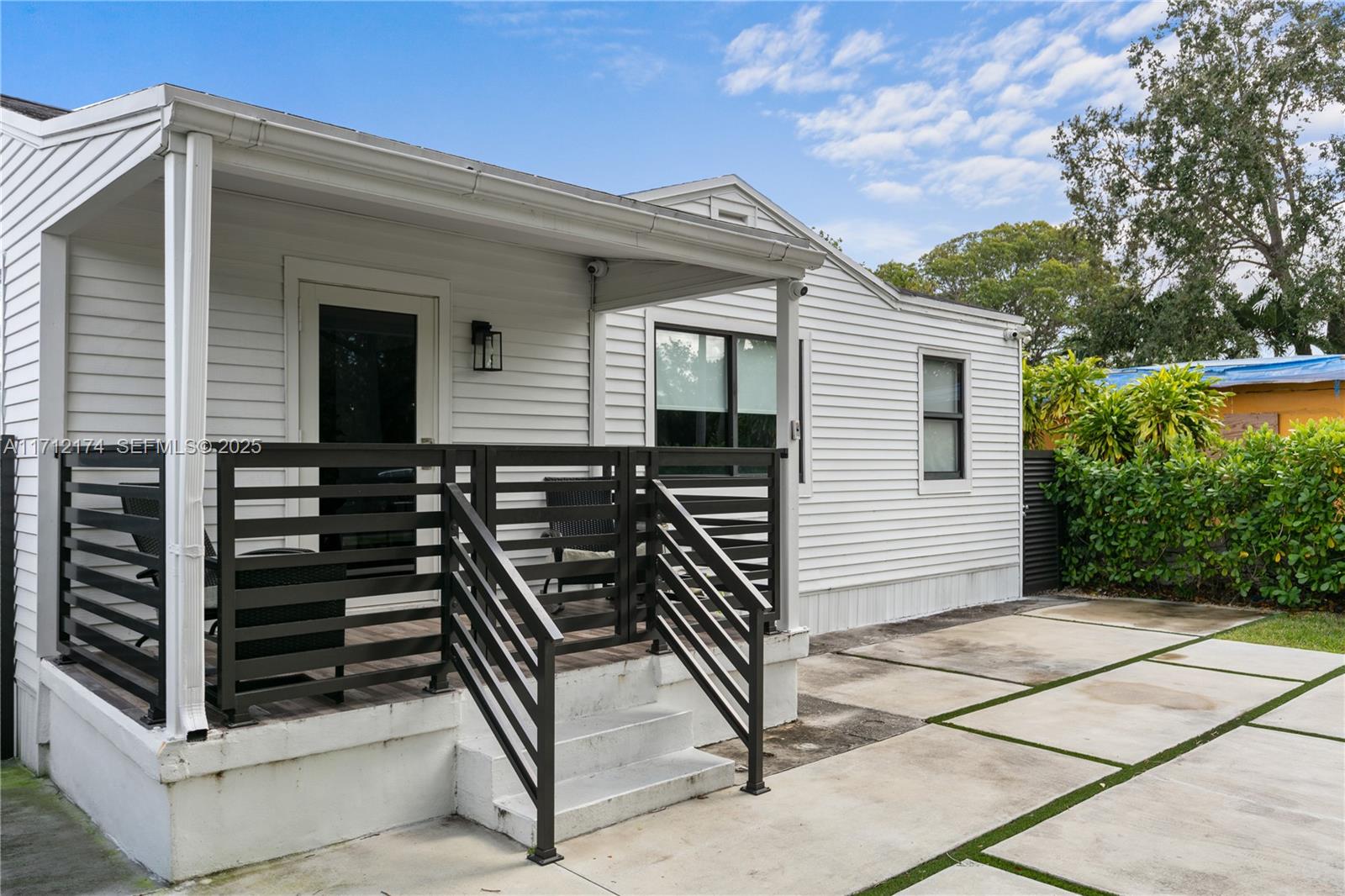 A white house exterior features a covered porch with black railings and concrete pavers — 341 NW 67th Ave, Miami Springs FL 33166, MIAMI SPRINGS, FL