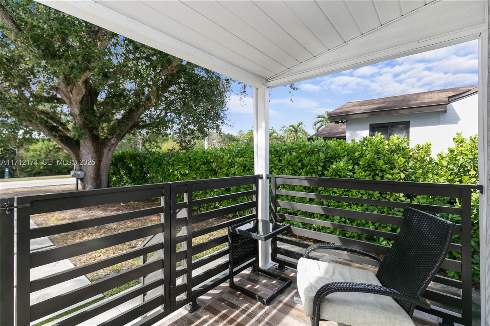 A covered patio features a black metal railing, a wicker chair, and a small side table — 341 NW 67th Ave, Miami Springs FL 33166, MIAMI SPRINGS, FL