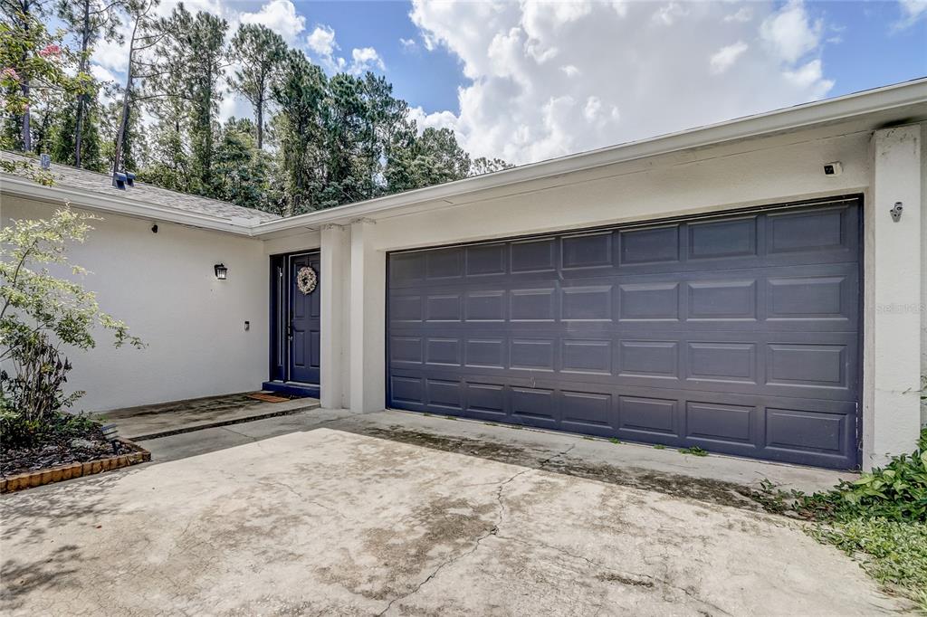 A white house exterior features a dark blue garage door and a matching front door — 8691 CONTOURA DRIVE, ORLANDO, FL