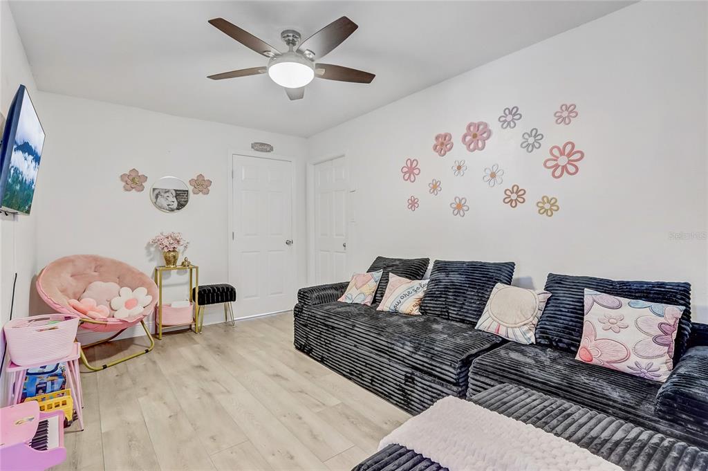 A living room features a dark gray sectional sofa, a pink accent chair, and floral wall decals — 8691 CONTOURA DRIVE, ORLANDO, FL