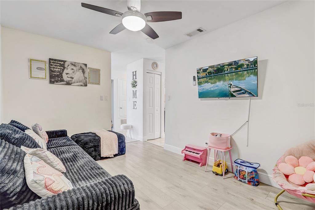 A living room features a dark gray sofa, a wall-mounted television, and light wood flooring — 8691 CONTOURA DRIVE, ORLANDO, FL