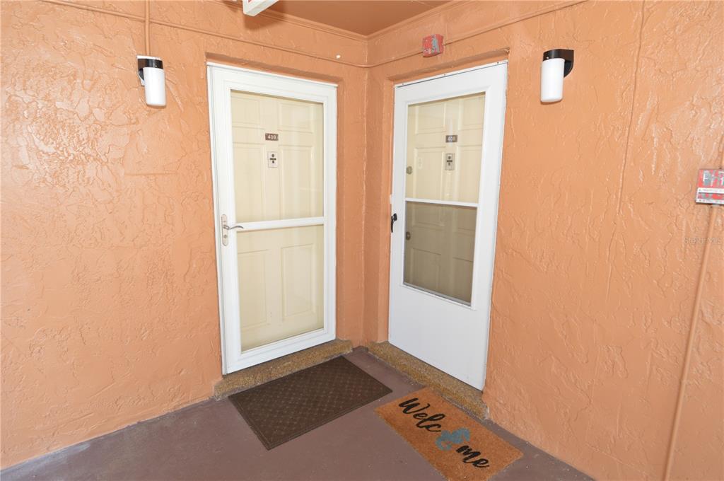 Two white storm doors with unit numbers are set into a textured, peach-colored exterior wall — 12760 INDIAN ROCKS ROAD UNIT 409, LARGO, FL