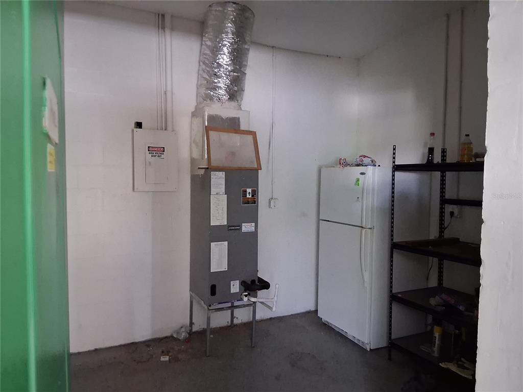 A utility room features a furnace, a white refrigerator, and metal shelving against white walls — 11470 CR 727, WEBSTER, FL
