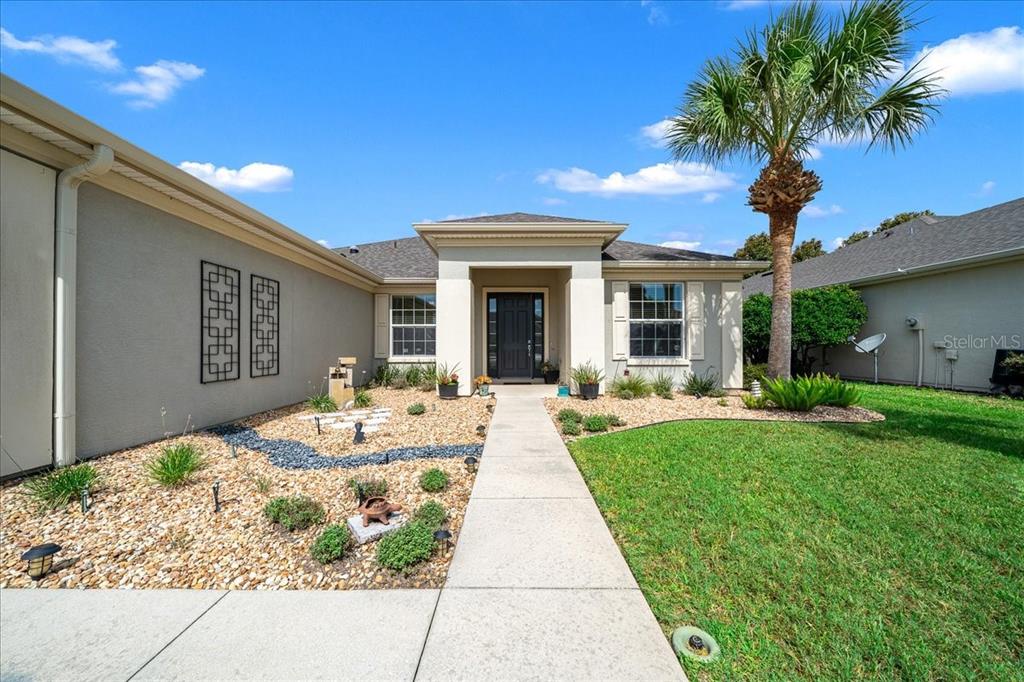 The exterior of a single-story house features a concrete walkway, rock landscaping, and a palm tree — 7338 SW 94TH COURT, OCALA, FL