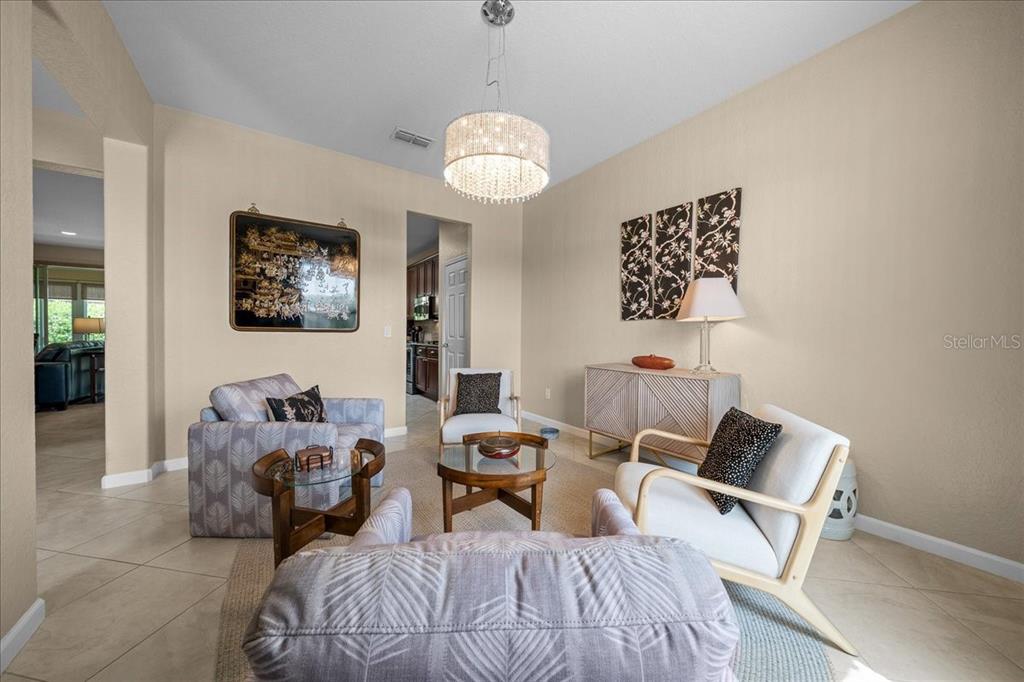 A living room features a crystal chandelier, patterned armchairs, a glass coffee table, and artwork — 7338 SW 94TH COURT, OCALA, FL
