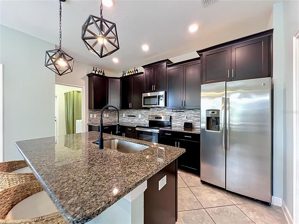 A kitchen features dark wood cabinets, granite countertops, stainless steel appliances, and geometric pendant lights — 11780 STEIN STREET, ORLANDO, FL