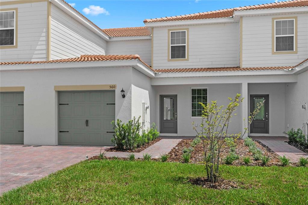 A two-story townhouse exterior features a gray garage, a paved walkway, and a small lawn — 560 BAY LEAF DRIVE, POINCIANA, FL