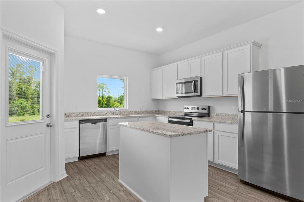 A kitchen features white cabinets, granite countertops, stainless steel appliances, and a central island — 560 BAY LEAF DRIVE, POINCIANA, FL