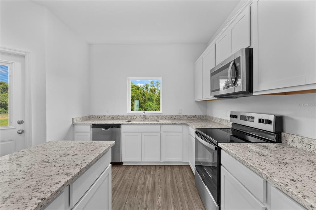 A kitchen features white cabinets, granite countertops, stainless steel appliances, and wood-look flooring — 560 BAY LEAF DRIVE, POINCIANA, FL
