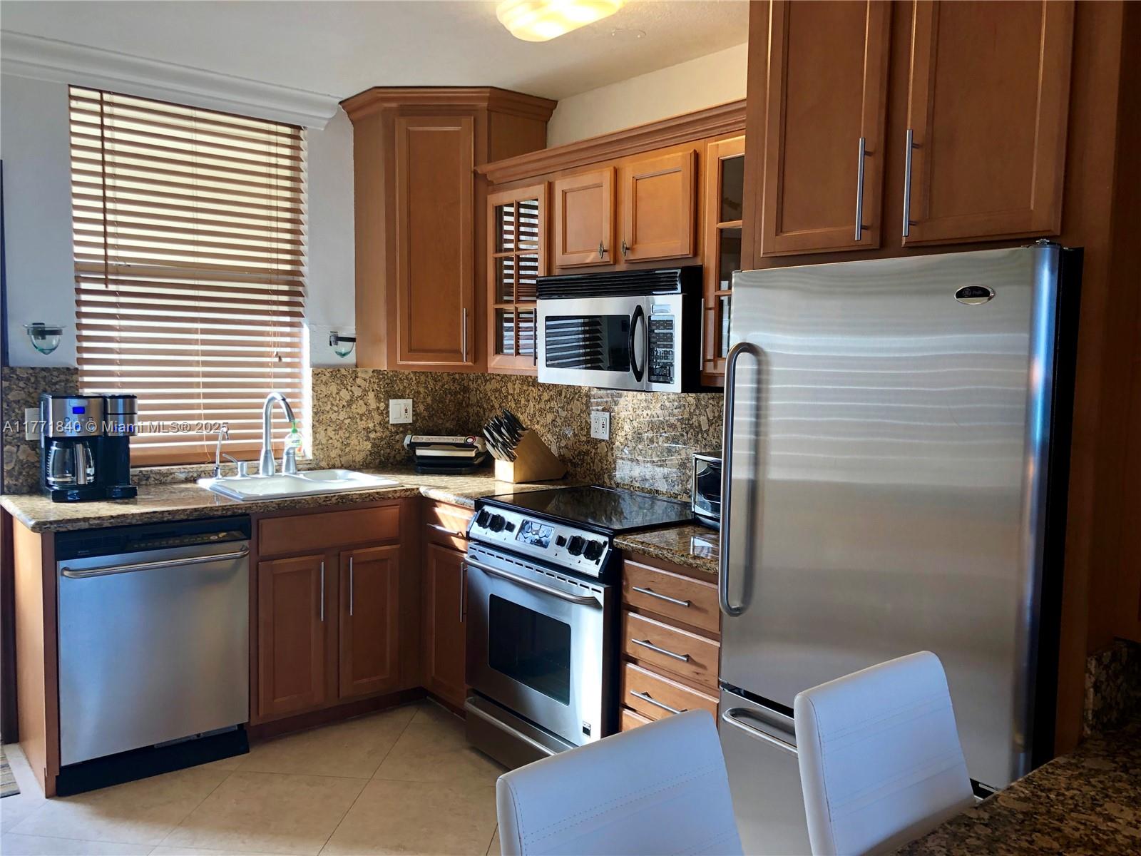 A kitchen features wood cabinets, stainless steel appliances, granite countertops, and a window with blinds — 1936 S Ocean Dr # 24C, Hallandale Beach FL 33009, HALLANDALE BEACH, FL