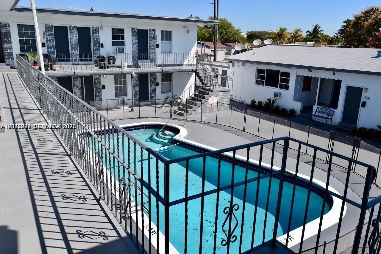 An outdoor swimming pool is situated between two white apartment buildings with metal railings — 1843 Dewey St # 104, Hollywood FL 33020, HOLLYWOOD, FL