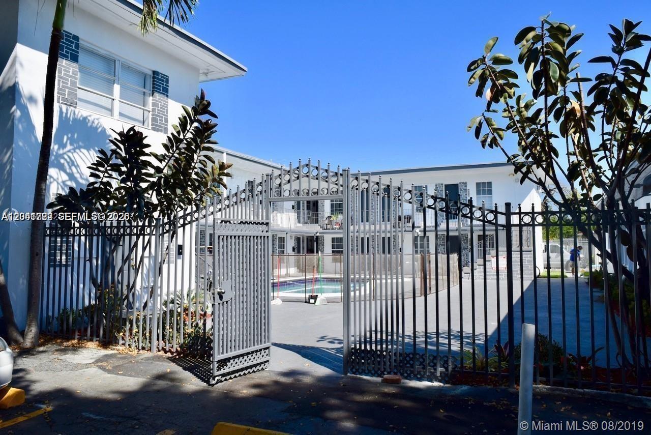 A gated entrance leads to a courtyard featuring a swimming pool and two-story apartment buildings — 1843 Dewey St # 104, Hollywood FL 33020, HOLLYWOOD, FL