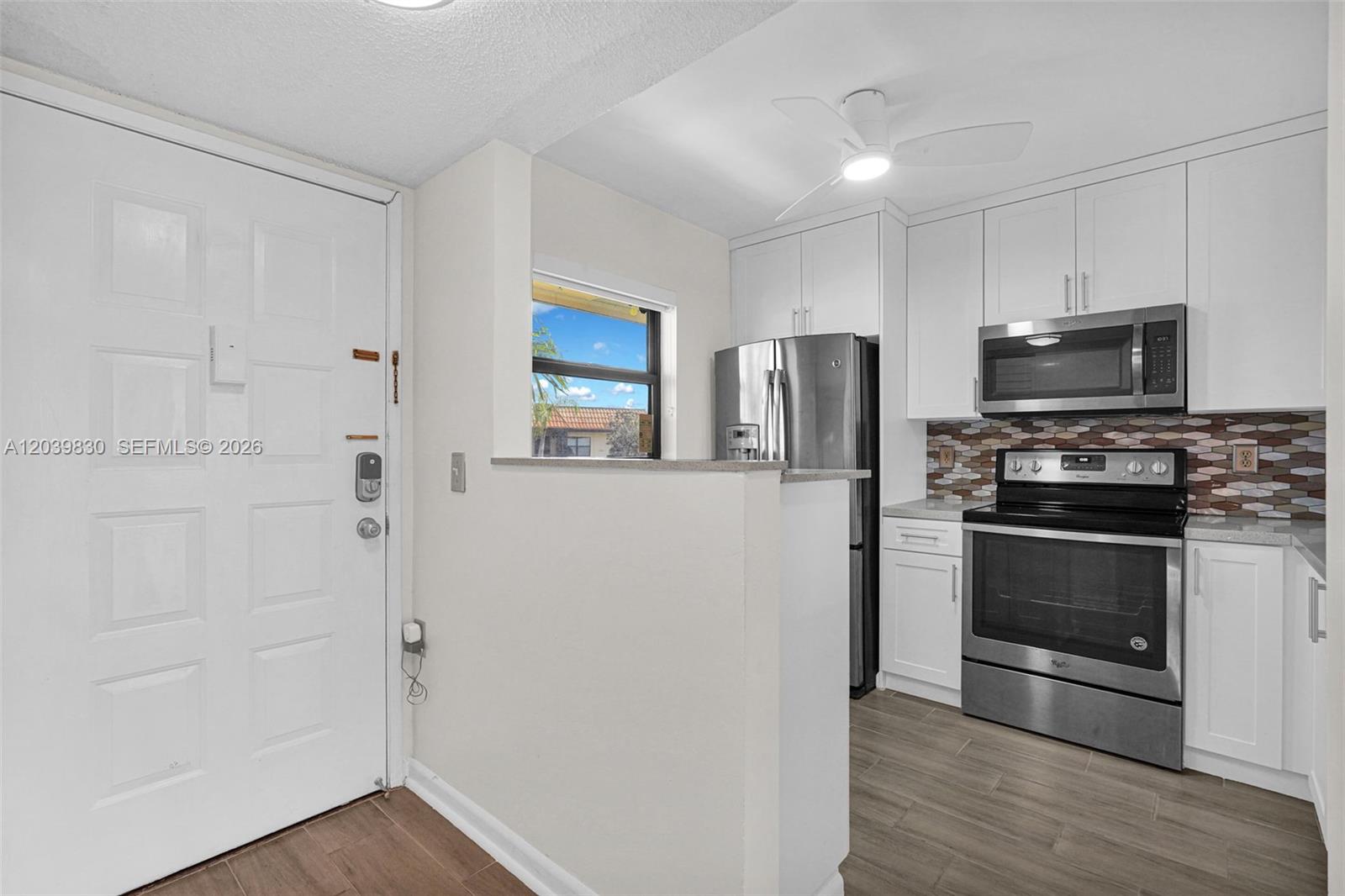 A kitchen features white cabinets, stainless steel appliances, a tiled backsplash, and a pass-through window — 7142 Golf Colony Ct # 206, Lake Worth FL 33467, LAKE WORTH, FL