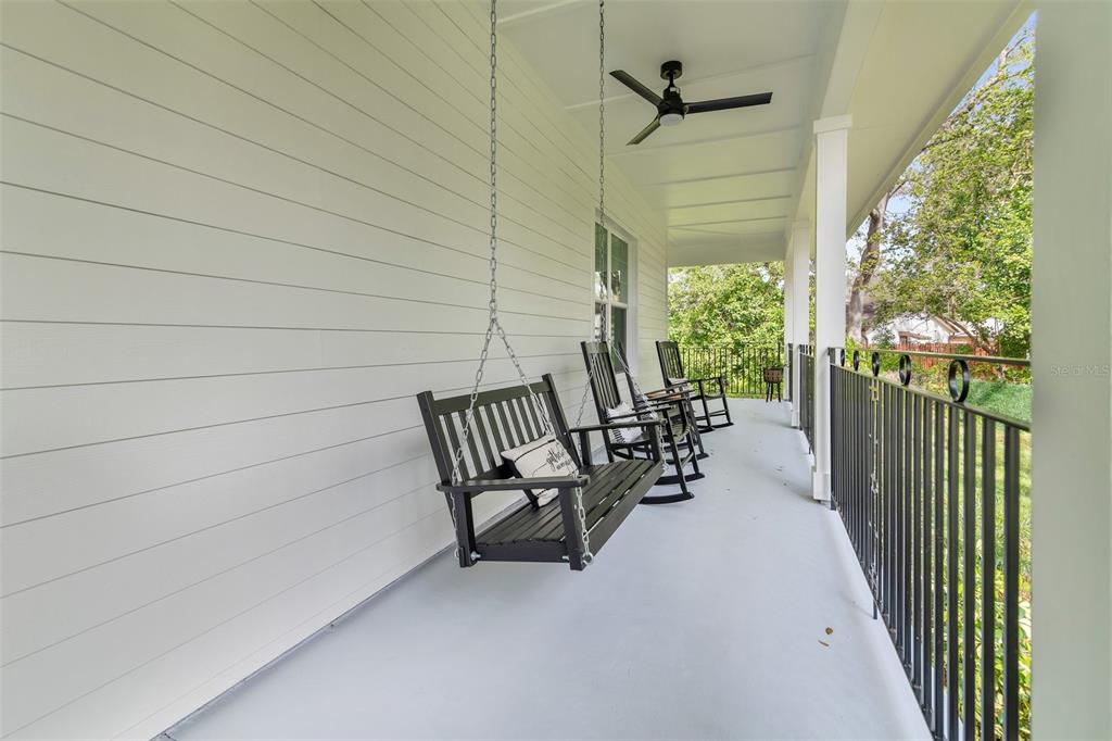 A covered porch features a hanging black bench, rocking chairs, and a ceiling fan — 599 GLENDEVON DRIVE, NEW SMYRNA BEACH, FL