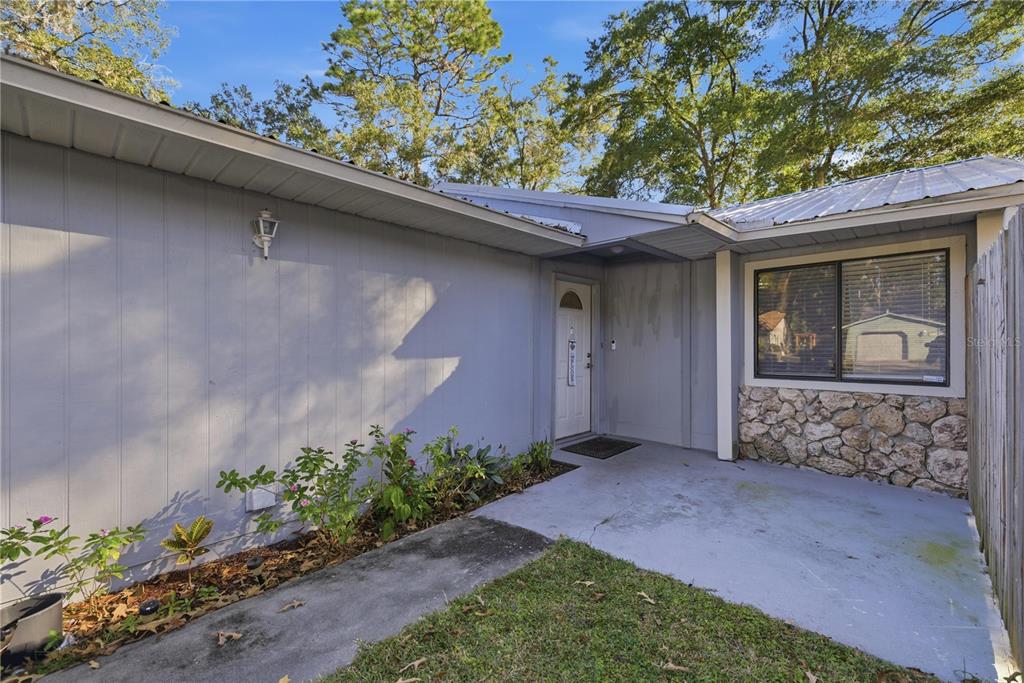 A gray house exterior features a concrete walkway, a stone-accented wall, and a front door — 1939 SW 73RD TERRACE, GAINESVILLE, FL