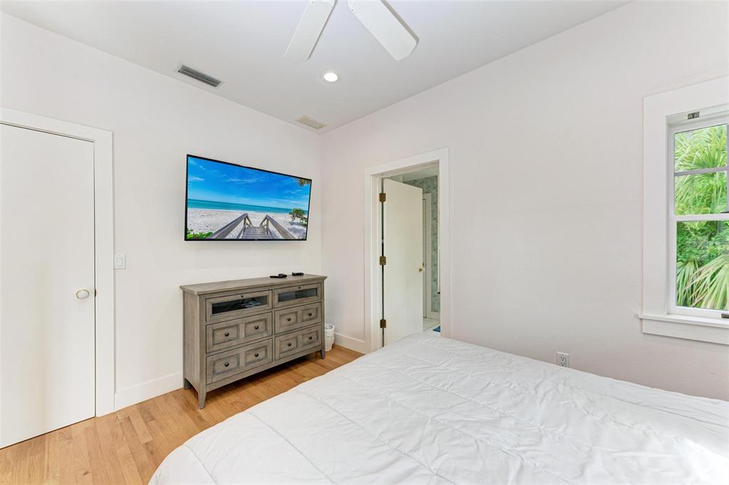 A bedroom features a wall-mounted television above a wooden dresser and a white bed — 7520 MANASOTA KEY ROAD, ENGLEWOOD, FL