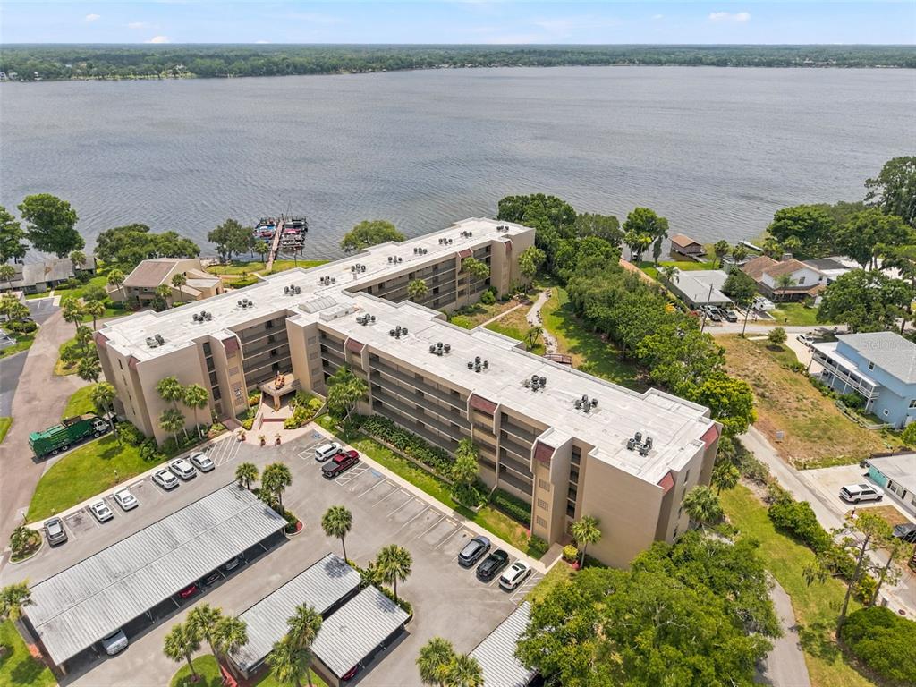 An aerial view shows a multi-story apartment building with a parking lot and lakefront access — 90 S HIGHLAND AVENUE UNIT 1414, TARPON SPRINGS, FL