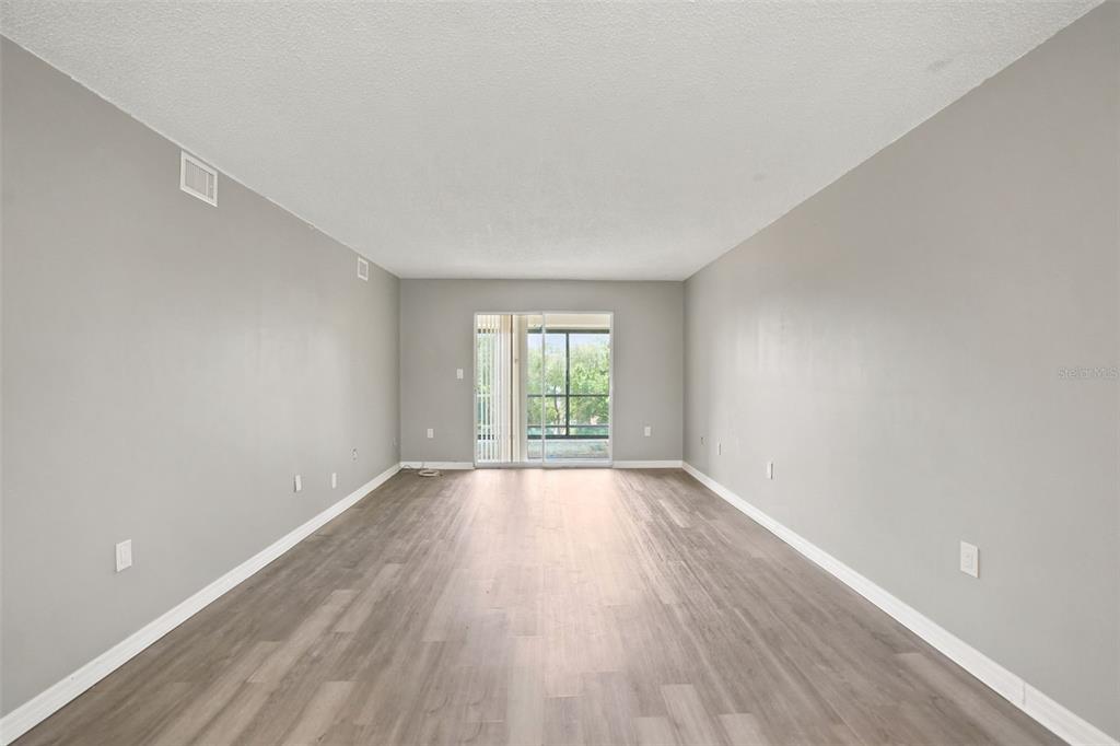 An empty living room features light gray walls, wood-look flooring, and a sliding glass door — 90 S HIGHLAND AVENUE UNIT 1414, TARPON SPRINGS, FL