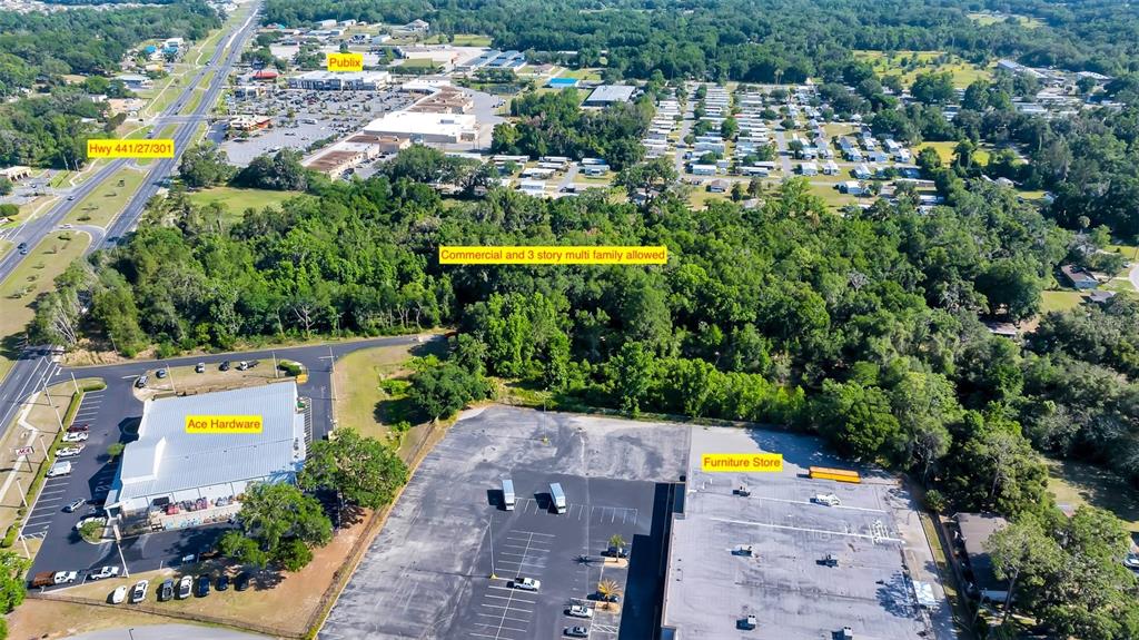 This aerial view shows a wooded lot situated between a shopping center and commercial buildings — 4799 SE 106TH PLACE ROAD, BELLEVIEW, FL