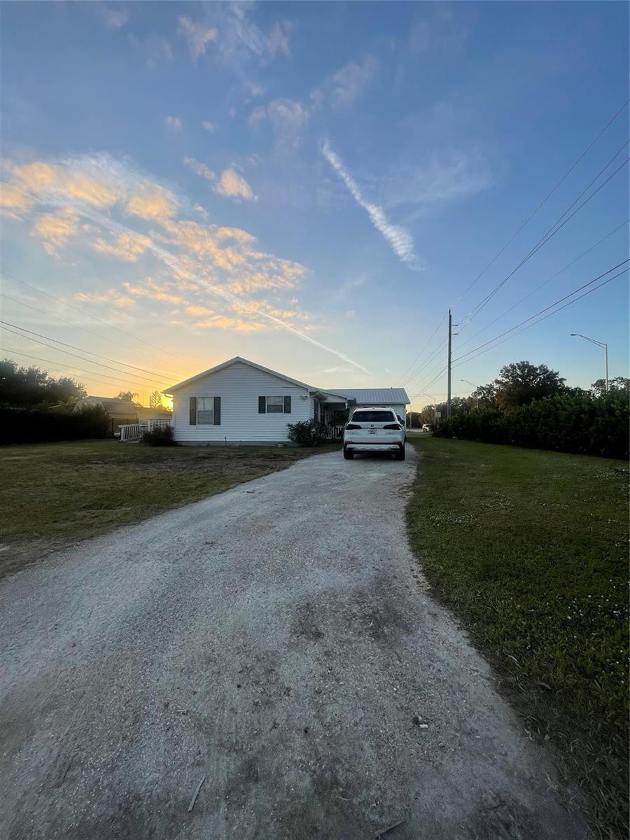 A white single-story house with a gravel driveway and a parked SUV at sunset — 2130 State Road 70, Okeechobee FL 34972, OKEECHOBEE, FL
