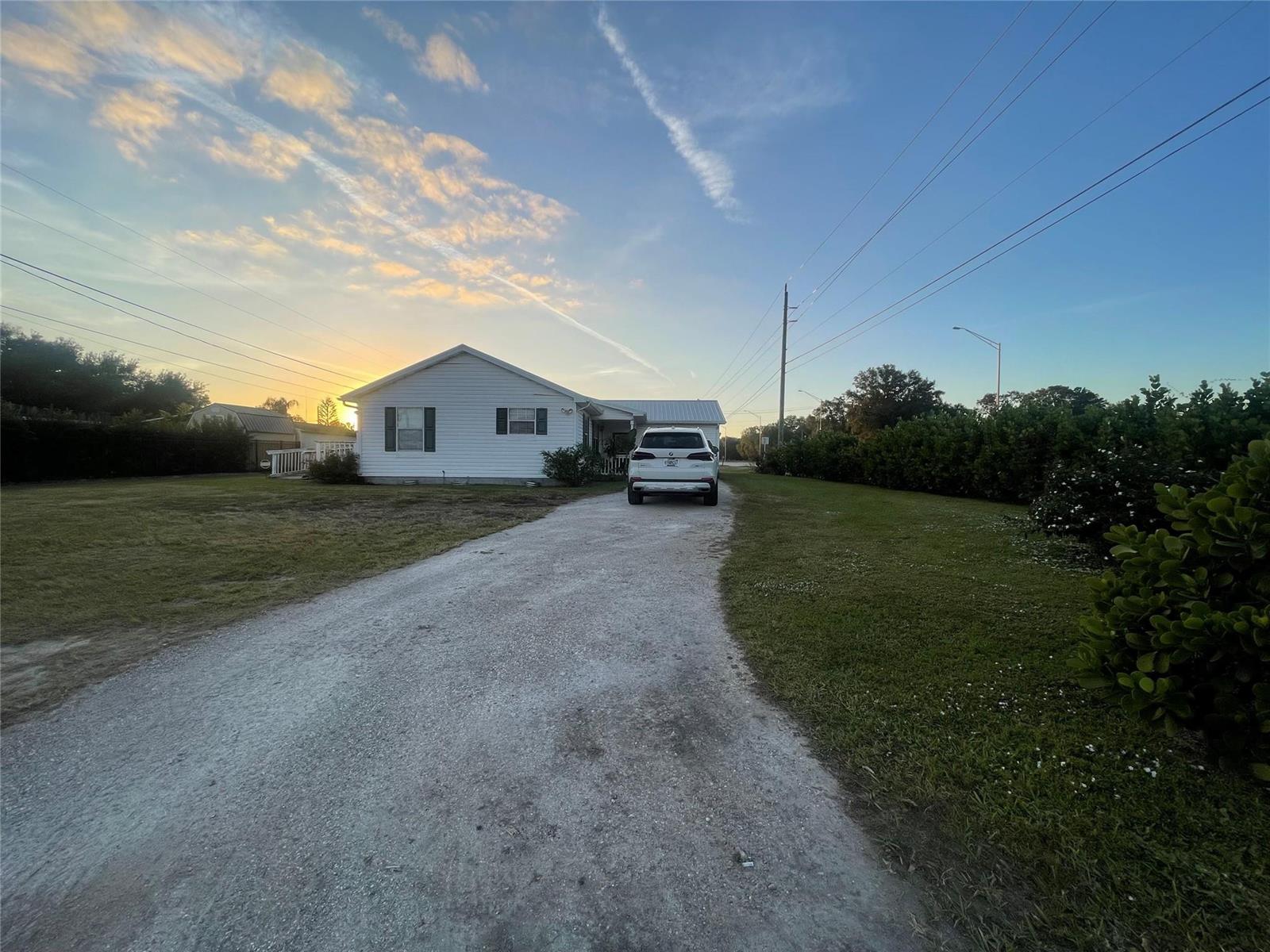 A white house with a gravel driveway and a parked SUV at sunset — 2130 State Road 70, Okeechobee FL 34972, OKEECHOBEE, FL