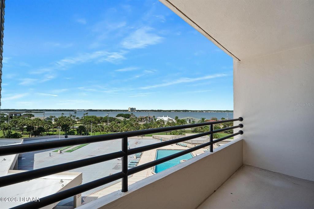 A balcony overlooks a swimming pool, green space, and a large body of water — 1 OCEANS WEST BOULEVARD UNIT 5A5, DAYTONA BEACH, FL