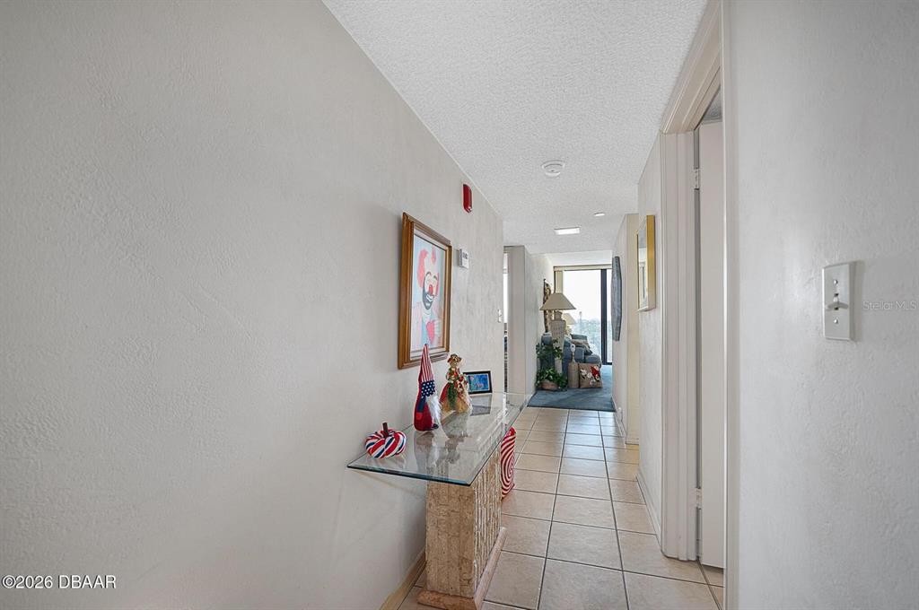 A tiled hallway features a glass console table, wall art, and a view into a living area — 1 OCEANS WEST BOULEVARD UNIT 5A5, DAYTONA BEACH, FL