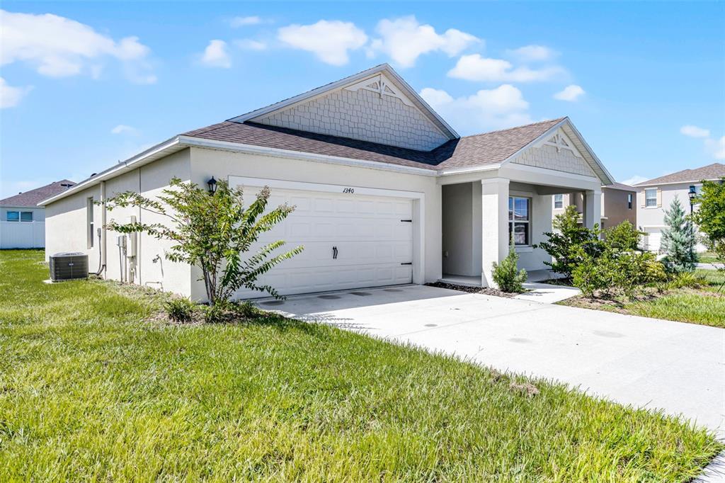 A single-story house with a white garage, beige stucco siding, and a concrete driveway — 1340 DAISY FIELD DR, WINTER HAVEN, FL
